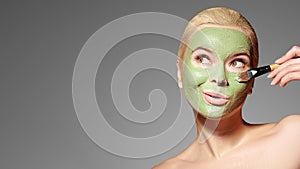 Beautiful Woman Applying Green Facial Mask. Beauty Treatments. Spa Girl Apply Clay Facial mask on grey background