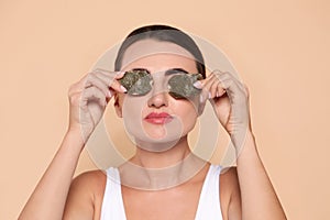 Beautiful woman applying green tea bags on skin under eyes against beige background