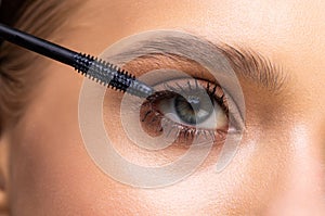 Beautiful woman applying mascara on her eyelashes isolated on white