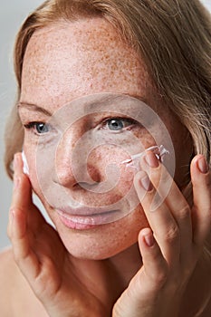 Beautiful woman applying moisturizer cream on her face