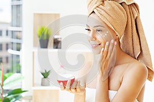 Beautiful woman applying moisturizer cream on her face.