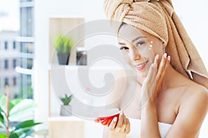 Beautiful woman applying moisturizer cream on her face.