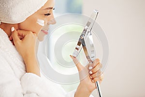 Beautiful woman applying moisturizer cream on her face.