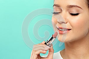 Beautiful woman applying nude lipstick on color background.