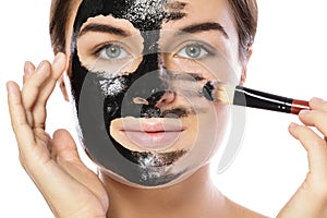 Beautiful woman is applying purifying black mask on her face