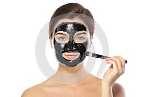 Beautiful woman is applying purifying black mask on her face