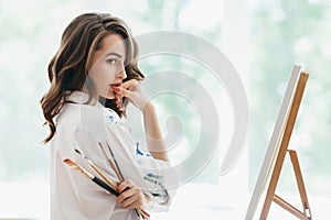 Beautiful woman artist with brushes posing in her studio