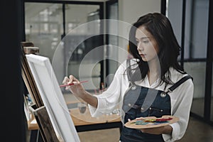 Beautiful woman artist painting in art studio with water color on canvas.