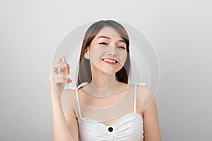 A beautiful woman of Asian appearance smiles into the camera and holds in her hand a jar of liquid with a scent of charm perfume