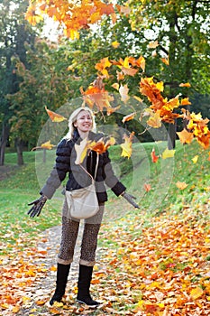 The beautiful woman in autumn park throws up red maple leaves in a sunny day