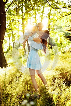 Beautiful woman with baby girl walking at the park, lovely mother kissing adorable daughter, caring parent lift in air