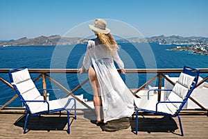 Beautiful woman from back in swimsuit white dress and straw hat on white terrace balcony of house or hotel with Sea View