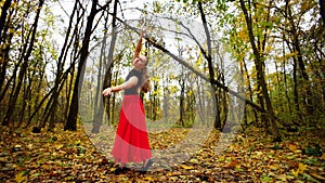 A beautiful woman in a ball gown moves in a dance in an autumn landscape.