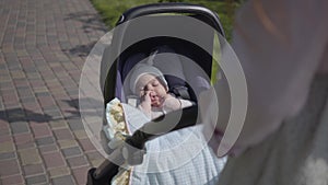 Beautiful woman bent over a pram in the park. The lady enjoying the sunny day with her baby outdoors. Young mother