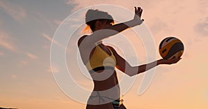 A beautiful woman in a bikini with a ball at sunset is getting ready to do serve jump on the beach in a volleyball match