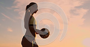 A beautiful woman in a bikini with a ball at sunset is getting ready to do serve jump on the beach in a volleyball match