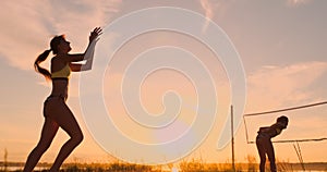 A beautiful woman in a bikini with a ball at sunset is getting ready to do serve jump on the beach in a volleyball match