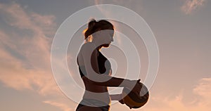 A beautiful woman in a bikini with a ball at sunset is getting ready to do serve jump on the beach in a volleyball match
