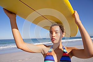 Beautiful woman in bikini carrying the surfboard on her head at beach in the sunshine