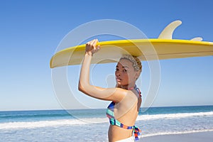 Beautiful woman in bikini carrying the surfboard on her head at beach in the sunshine