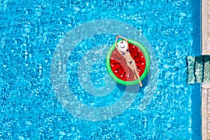 A beautiful woman in bikini takes a sunbath on a watermelon shaped float over blue pool water