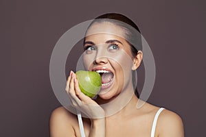 Beautiful woman biting green apple and smiling on brown background