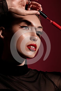 Beautiful woman in black clothes, classic make-up and red lips posing with lipstick in the studio.