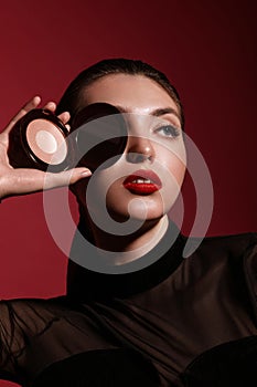 Beautiful woman in black clothes, classic make-up and red lips posing with powder in the studio.