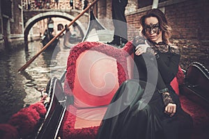 Beautiful woman in black dress with carnaval mask riding on gondola.