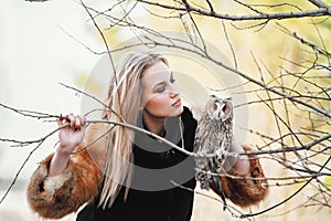 Beautiful woman in a black dress with an owl on his arm. Blonde with long hair in nature holding a owl. Romantic delicate girl