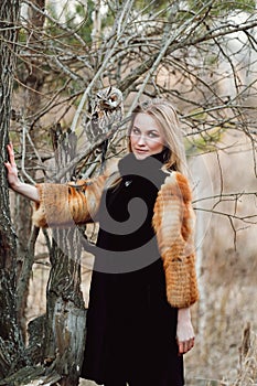 Beautiful woman in a black dress with an owl on his arm. Blonde with long hair in nature holding a owl. Romantic delicate girl