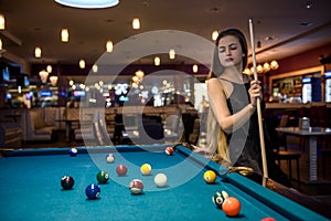 Beautiful woman in black dress posing with billiard cue