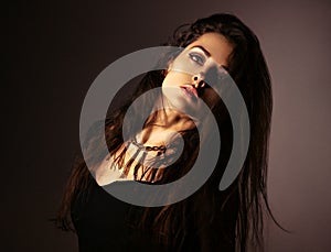 Beautiful woman in black dress posing in fashion necklace on the neck. Long hairstyle on dark shadow background. Toned portrait