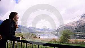 Beautiful woman in a black dress smiling at sunset on a background of mountains and a lake. Laughing girl in a balcony with cloudy