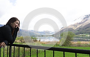 Beautiful woman in a black dress smiling at sunset on a background of mountains and a lake. Laughing girl in a balcony with cloudy