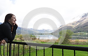 Beautiful woman in a black dress smiling at sunset on a background of mountains and a lake. Laughing girl in a balcony with cloudy