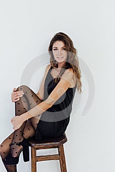 Beautiful fashionable woman in black dress and tights sits on a chair photo