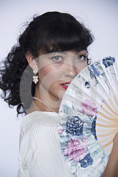 Beautiful woman with black hair and oriental floral fan with earrings and white lace dress modeling portrait