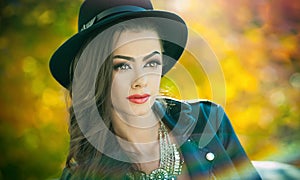 Beautiful woman with black hat posing in autumnal park. Young brunette spending time during autumn in forest