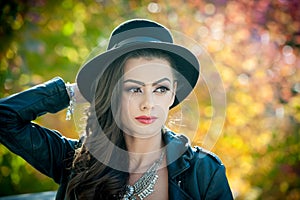 Beautiful woman with black hat posing in autumnal park. Young brunette spending time during autumn in forest