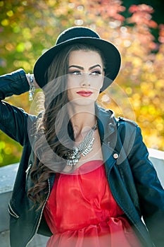 Beautiful woman with black hat posing in autumnal park. Young brunette spending time during autumn in forest