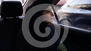 Beautiful woman in black hijab sitting on the backseat in the car and curiously looking on the street while the road