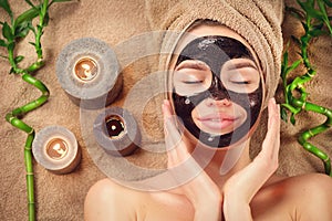Beautiful woman with black purifying black mask on her face. Beauty model girl with black facial peel-off mask lying in spa salon