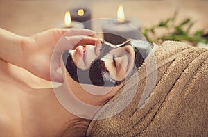 Beautiful woman with black purifying black mask on her face. Beauty model girl with black facial peel-off mask lying in spa salon