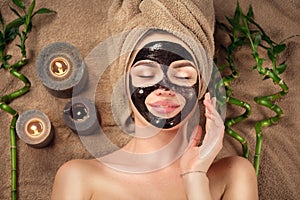 Beautiful woman with black purifying black charcoal mask on her face. Beauty model girl with black facial peel-off mask photo