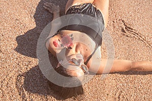 Beautiful woman in a bathing suit lying on the sand by the sea top view