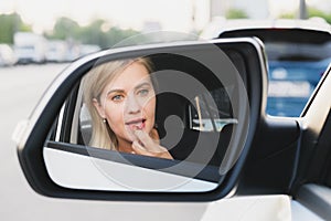 Beautiful woman with blond hair driving a car paints her lips with lipstick