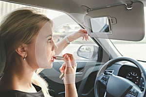 Beautiful woman with blond hair driving a car paints her lips with lipstick