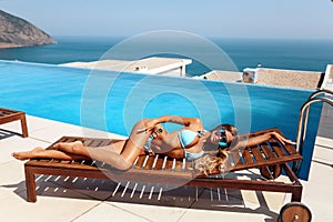 Beautiful woman with blond hair in elegant bikini posing near swimming pool with sea view