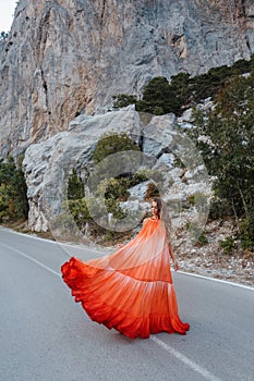 Beautiful woman with blond hair in elegant clothes posing on the road with mountains view